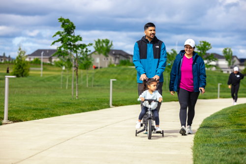 A mother, father, and small girl with a bike walk through Reed’s Crossing Park in Hillsboro, Oregon.