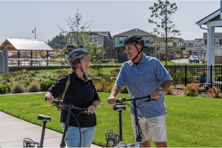 Two older adults on a bike ride along the Reed’s Crossing greenway under blue skies.