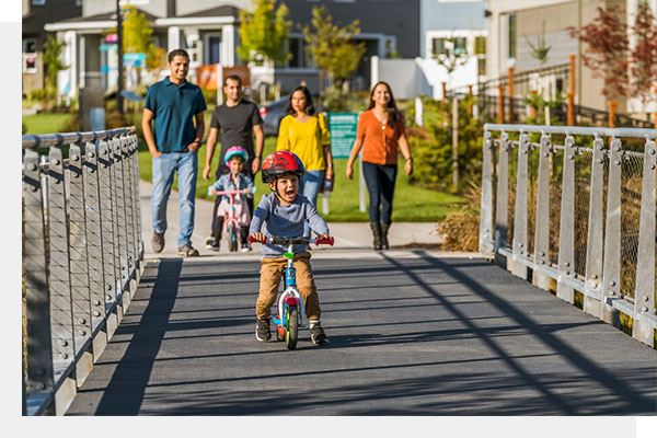 Children riding a bike across a bridge with family Reeds Crossing Community Hillsboro OR