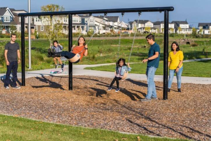 Two families with young children swing on a swing set.