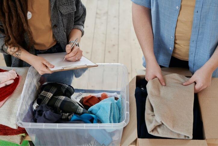 Two people putting together a care package of clothing and home essentials.