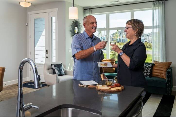 A middle-aged couple drinks wine in their kitchen.