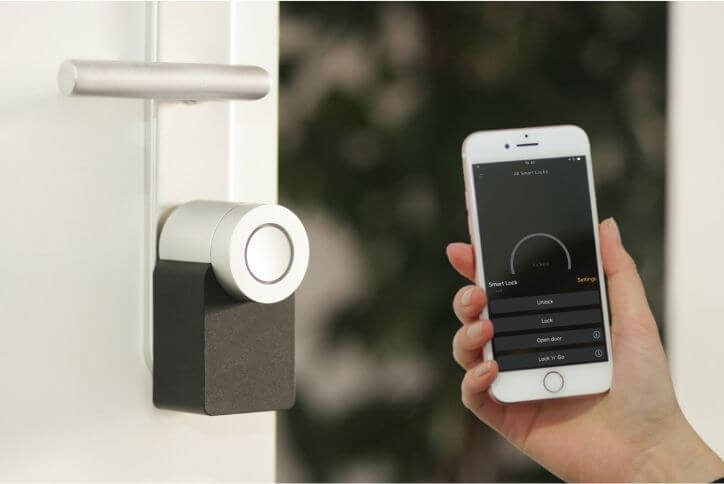 A person holds a smartphone up next to a smart door lock.