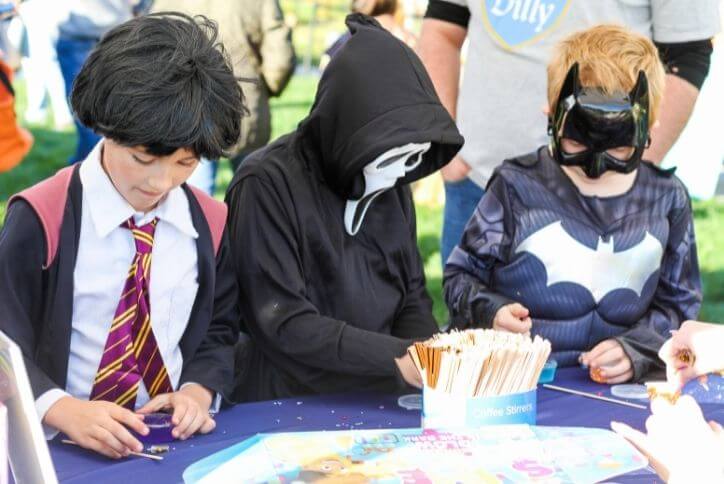 Three kids at community event in costumes playing with treats.