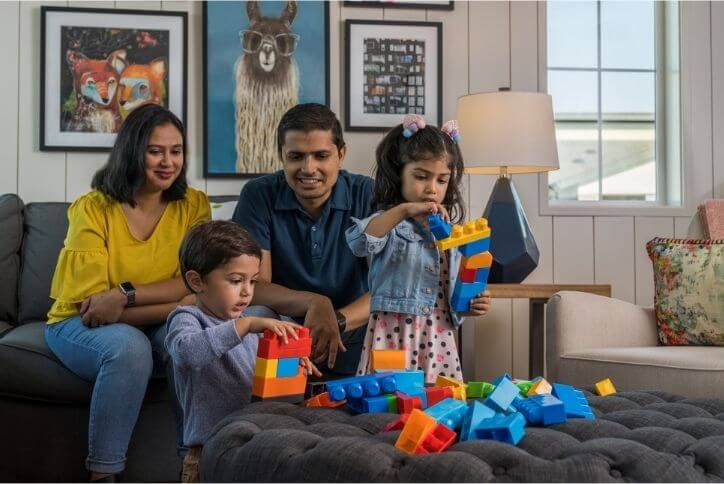 Family of four in new construction home whith children playing with large construction blocks.