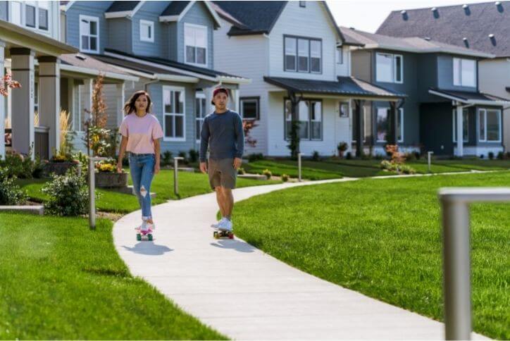 Two teens on skateboards riding on a path through a community.