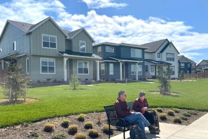 A couple sits on a bench in front of a row of new homes near Tamarack Park.