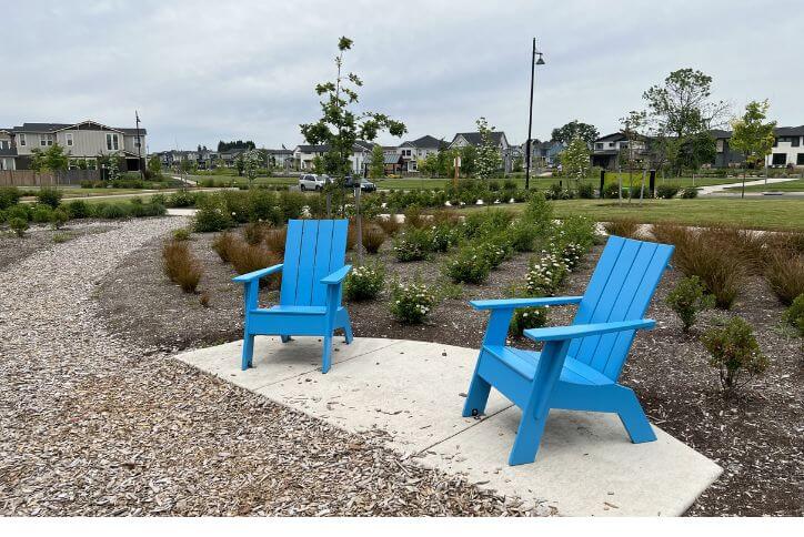 Two bright blue wood chairs along a bark chip path in a park at Reed’s Crossing.