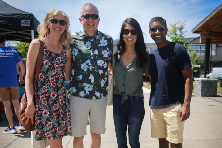 Four people pose for a photo at a community event on a sunny day.