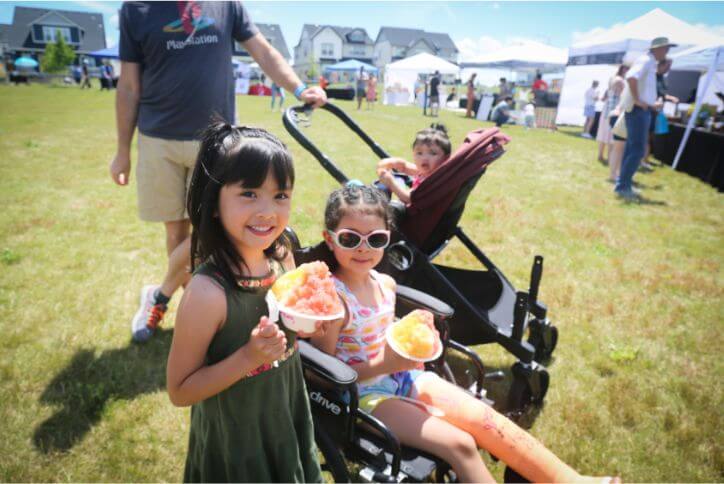 Two children enjoy cups of orange shaved ice at an event in Tamarack Park.