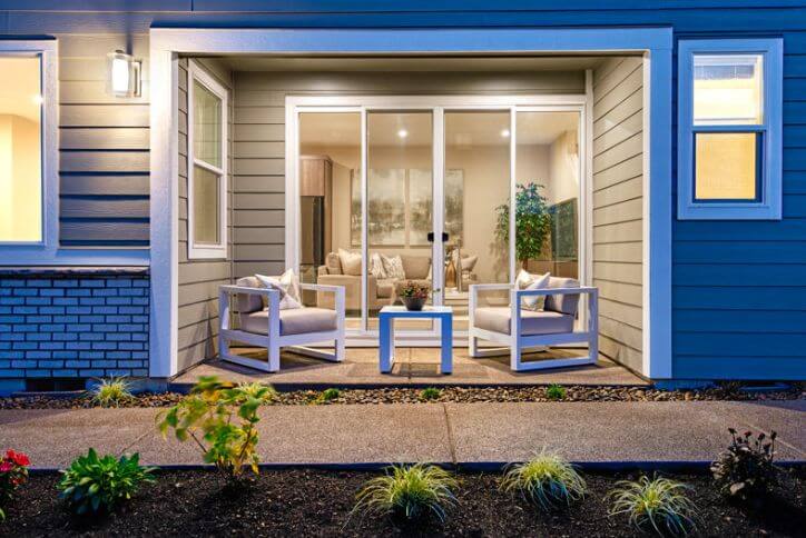 A cozy covered patio with two chairs, a table, and warm lighting glows at dusk in Reed’s Crossing.