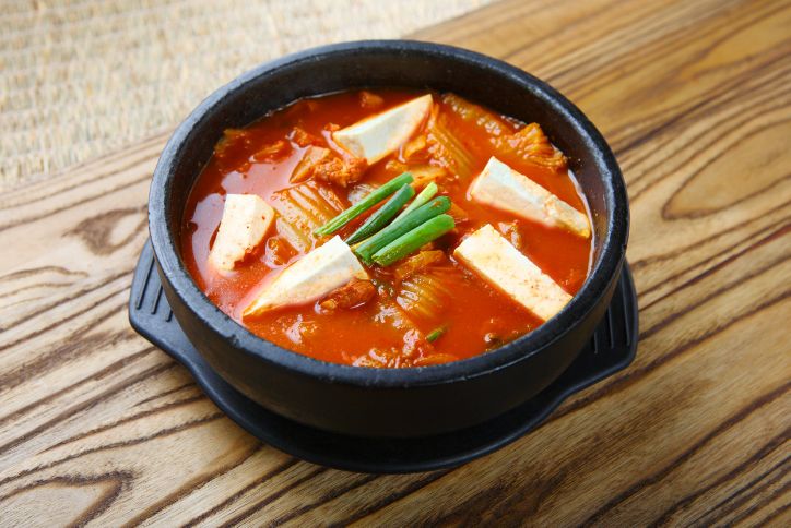 A bowl of kimchi jjigae with tofu and green onions.