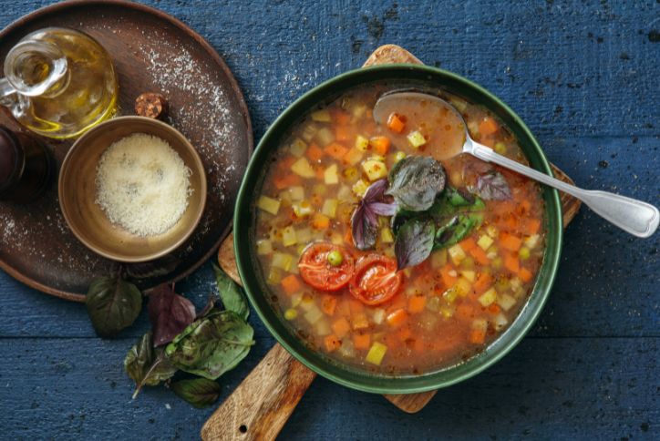 A bowl of minestrone and a bowl of shredded parmesan.