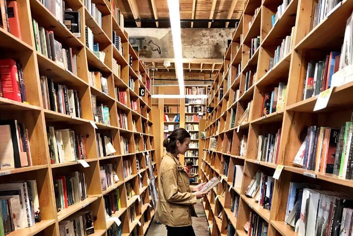 A reader dwarfed by tall bookshelves at Powell’s City of Books in Portland, OR.
