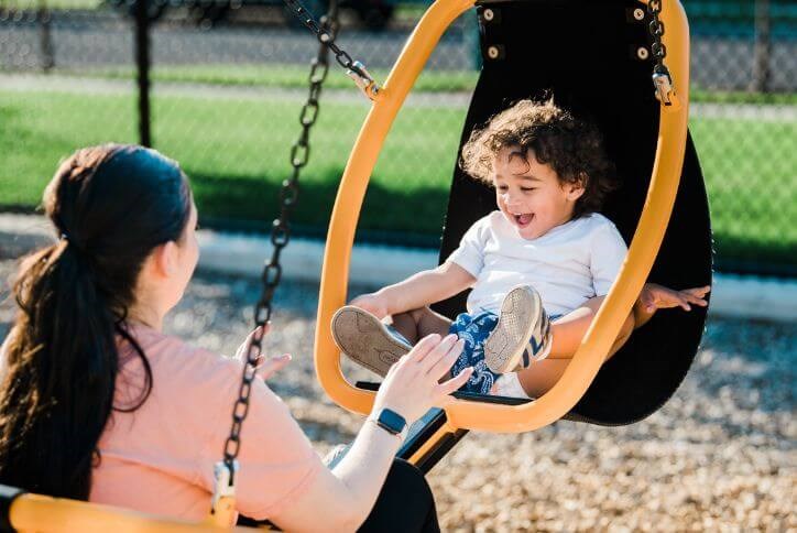 A laughing child and mother play on a swing set at Tamarack Park in Hillsboro, OR.