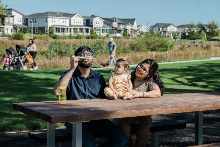 A young Indian couple blows soap bubbles at a baby in a park at Reed’s Crossing.