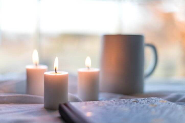 Three small candles in front of a blurred background showing a mug and window.