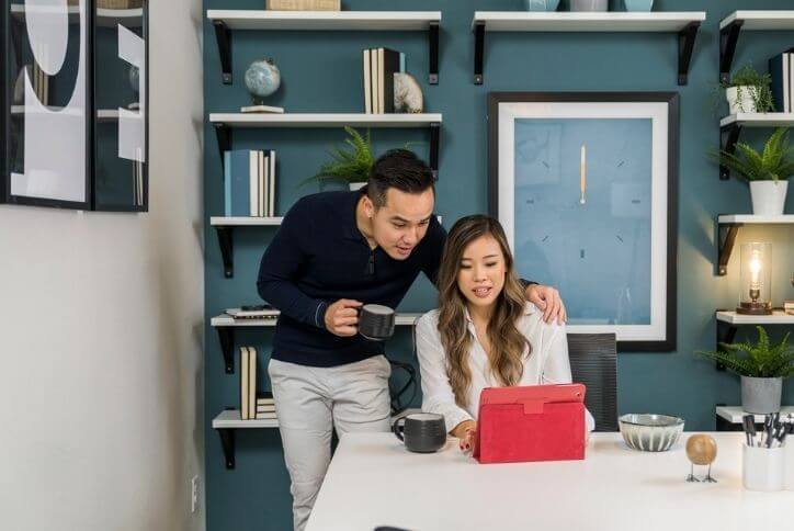 A young man and woman look at a red tablet computer.