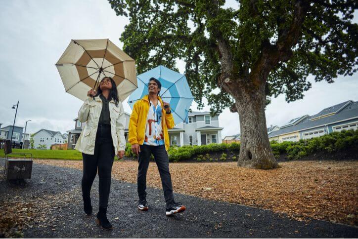 A man and woman carry umbrellas on a cloudy day in Hillsboro, Oregon’s Oak Grove Park.