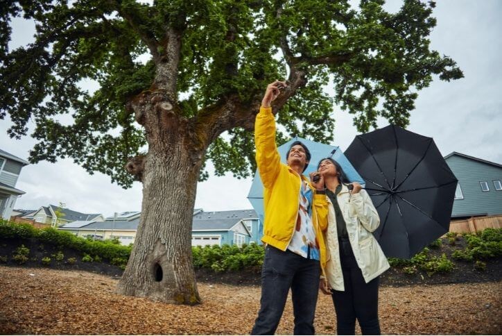 A young couple holding umbrellas poses for a rainy-day selfie at Reed’s Crossing in Oak Grove Park, Hillsboro.
