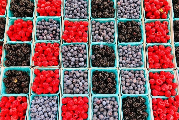 At a farmer’s market, pints of raspberries, blueberries, and blackberries look like a checkerboard.