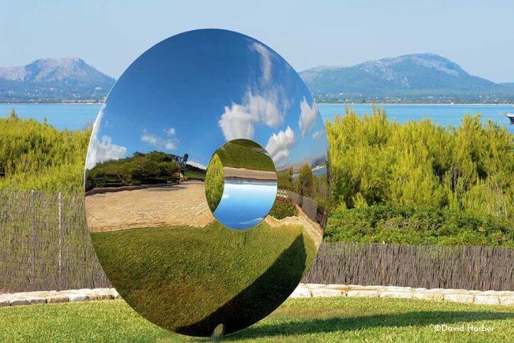 A rounded, mirrored steel sculpture reflects the grass and sky around it.