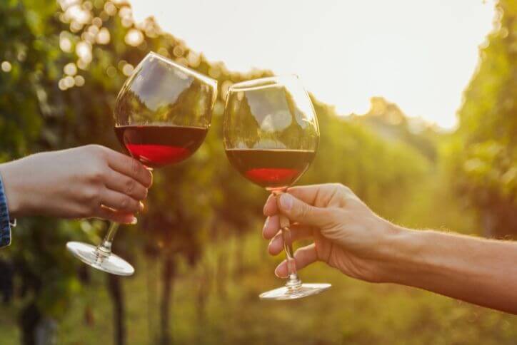 Close-up shot of people clinking together two wine glasses filled with red wine.