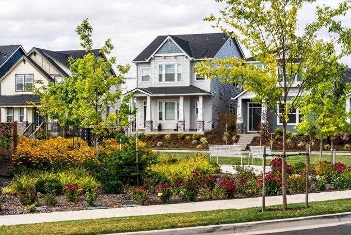 New homes in Hillsboro, Oregon face a park with trees, flowering bushes, and white benches.