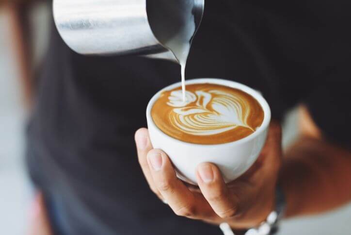 Close-up shot of milk pouring into a cup of espresso to form a design in the foam.