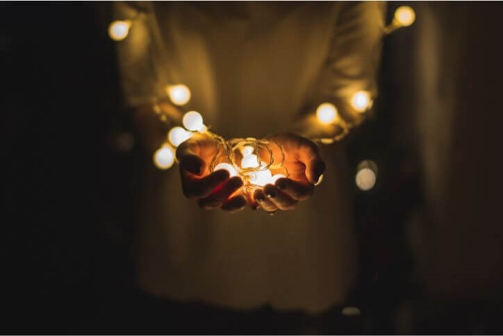 A person holds warm, glowing white string lights in their cupped hands.