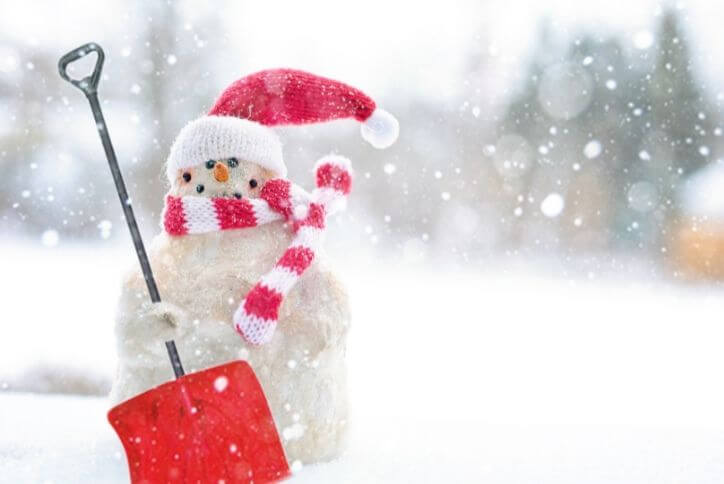 A snowman decorated with a red hat, striped scarf, and a red shovel.