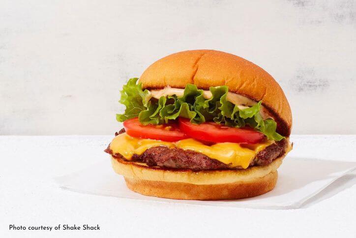 A Shake Shack burger with melted cheese, green lettuce, and red tomato.