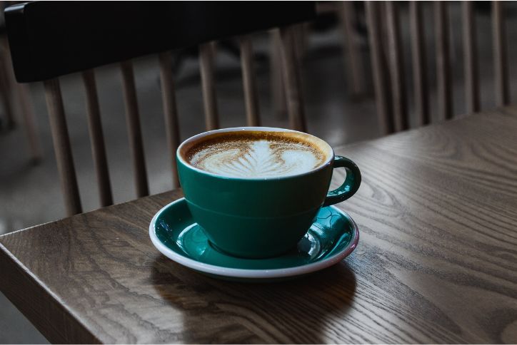Selective focus photo of a latte in a green mug on a dark wood table.