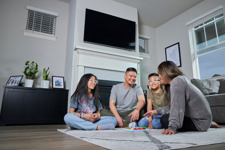 Two parents and their children play a board game on the living room floor in the Reed’s Crossing community.