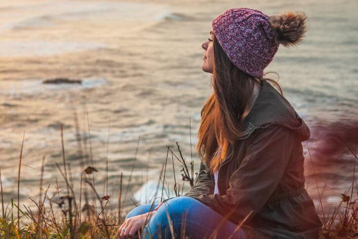 A woman in a purple beanie looks out at the Pacific coastline in Oregon.