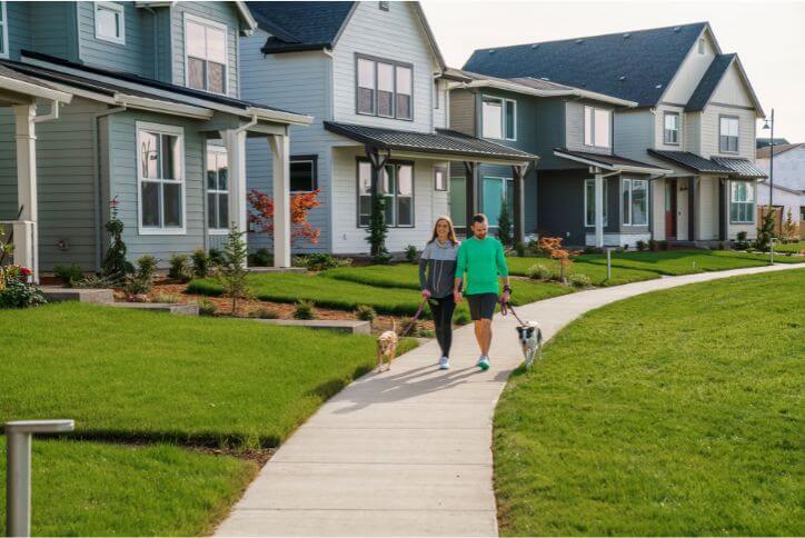 A man and woman walk two dogs in front of homes for sale in Hillsboro, Oregon.