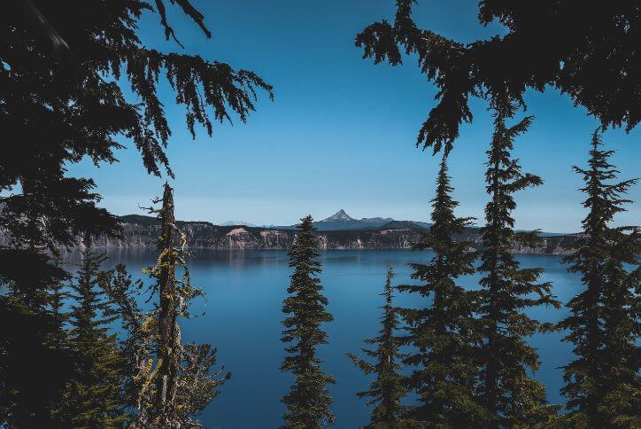 Green trees frame a blue lake, with a mountain peak visible in the background.