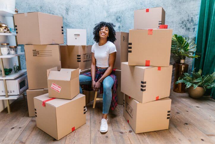 A young woman surrounded by moving boxes beams at the camera.