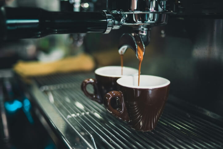 Close-up of an espresso machine dripping coffee into two brown coffee mugs.