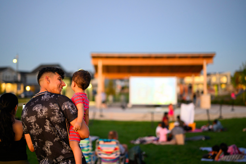 A man holds a small boy up in front of the screen at movie night in Reed’s Crossing Park.