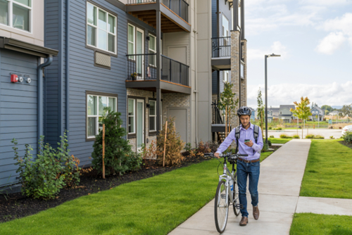 A man in business attire wheels a bike along a path at Reed’s Crossing in Hillsboro, Oregon.