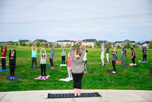 Reed’s Crossing residents stand and stretch in a guided yoga session at Reed’s Crossing Park.