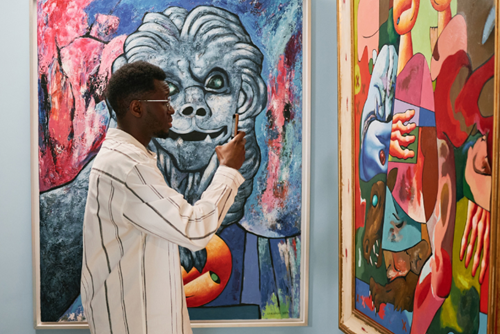 A man stands in an art gallery observing colorful modern paintings.