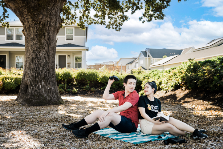 A man watches birds with binoculars and a woman reads a book in Oak Grove Park.