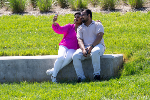 A couple sitting on a bench takes a selfie in Reed’s Crossing Park.