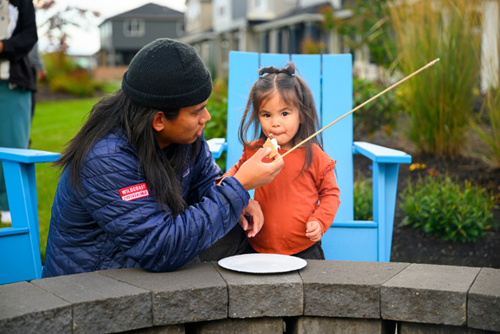 A father helps his daughter with a s’more at firepit night in Hillsboro, OR’s Reed’s Crossing.