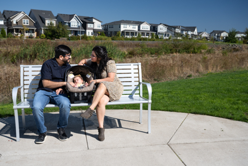 A couple and their baby sit on a bench in Dobbin Park at Reed’s Crossing.
