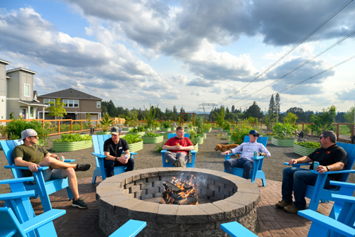 A group of men sit in Adirondack chairs around a fire pit in the Reed’s Crossing Community Garden.
