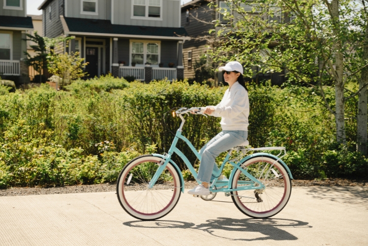  A woman rides a blue bicycle along a paved path in the Reed’s Crossing Greenway.